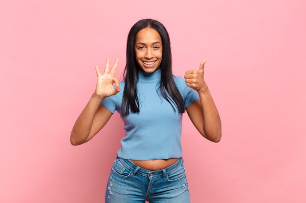 Young black woman feeling happy, amazed, satisfied and surprised, showing okay and thumbs up gestures, smiling