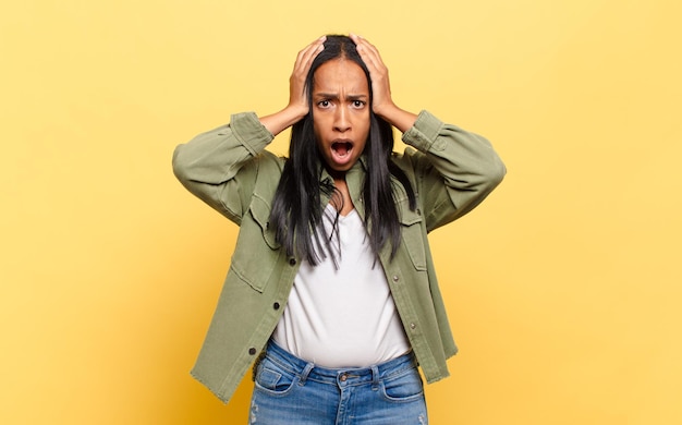 Young black woman feeling horrified and shocked, raising hands to head and panicking at a mistake