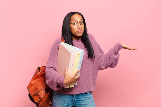 Young black woman feeling puzzled and confused, doubting, weighting or choosing different options with funny expression. student concept