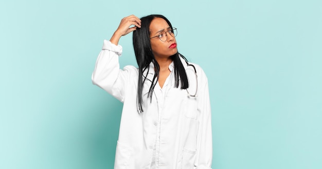젊은 흑인 여성은 어리둥절하고 혼란스러워서 머리를 긁적이며 옆을 바라보고 있습니다. 의사 개념