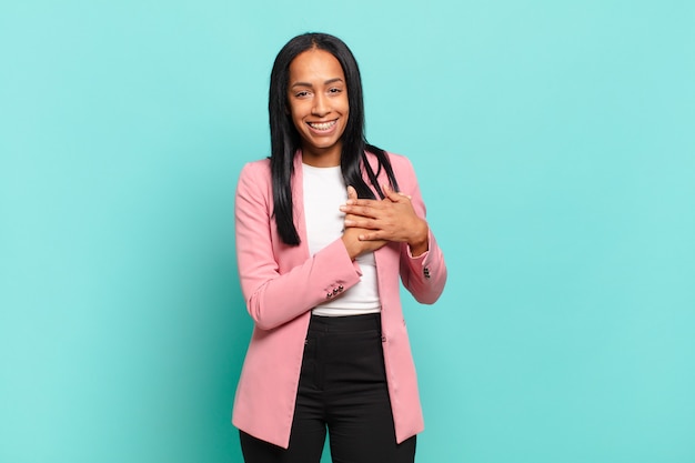 Young black woman feeling romantic, happy and in love, smiling cheerfully and holding hands close to heart. business concept