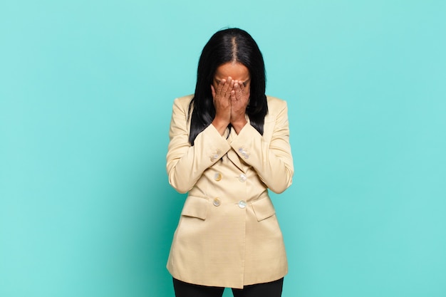 Photo young black woman feeling sad, frustrated, nervous and depressed, covering face with both hands, crying. business concept