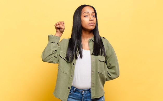 Young black woman feeling serious, strong and rebellious, raising fist up, protesting or fighting for revolution