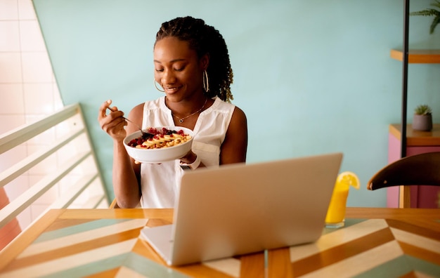 Young black woman having a healthy breakfast while working on laptop in the cafe