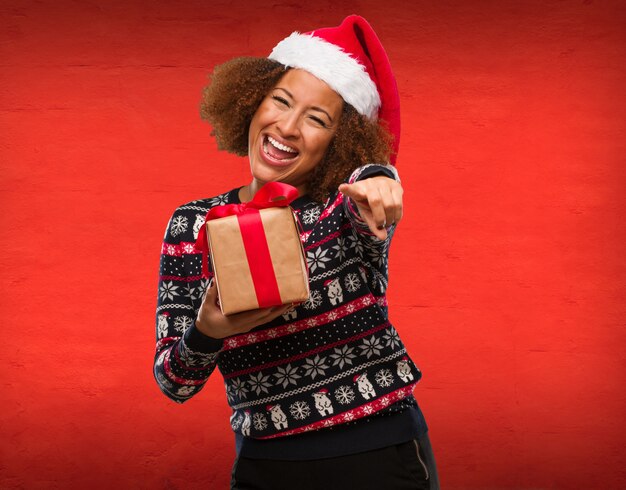 Giovane donna di colore che tiene un regalo nel giorno di natale allegro e sorridente