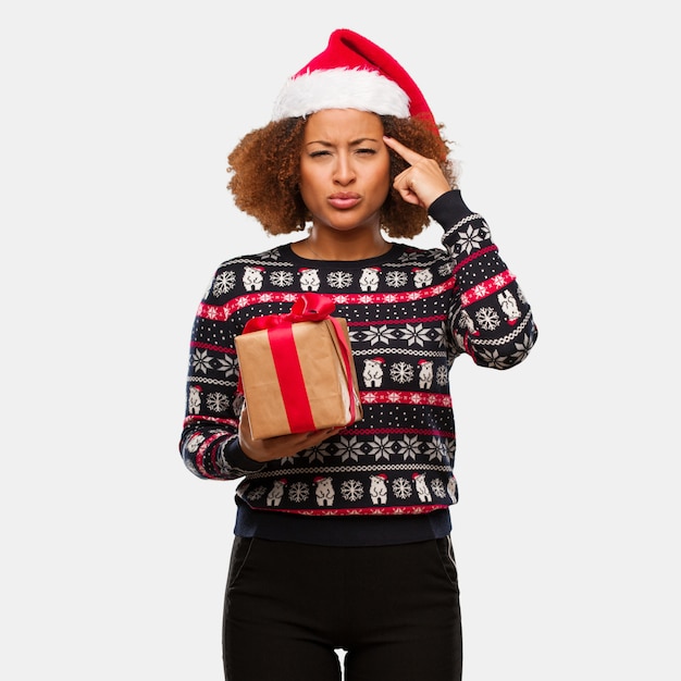 Young black woman holding a gift in christmas day doing a concentration gesture