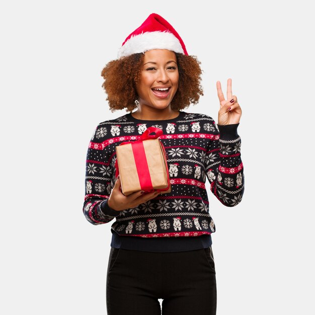 Young black woman holding a gift in christmas day fun and happy doing a gesture of victory