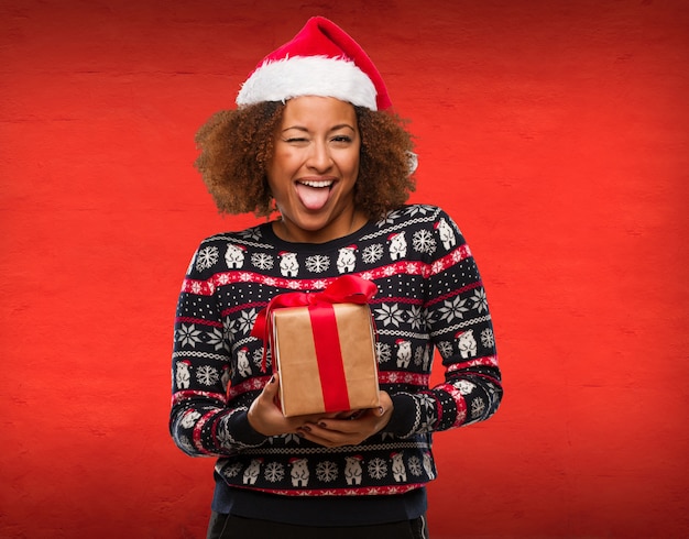 Молодая негритянка держит подарок в Рождество смешно и дружелюбно показывает язык