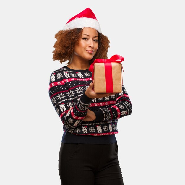 Young black woman holding a gift in christmas day looking straight ahead