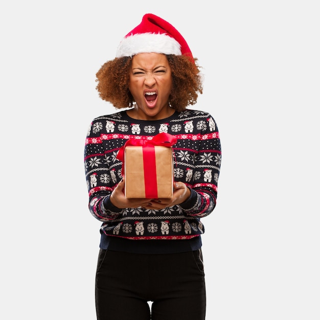 Young black woman holding a gift in christmas day screaming very angry and aggressive