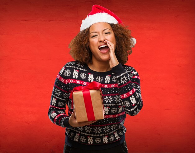 Young black woman holding a gift in christmas day shouting something happy to the front