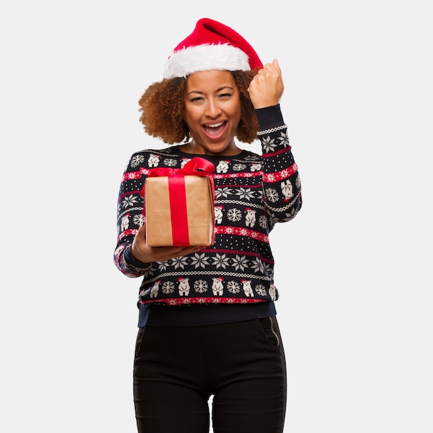 Young black woman holding a gift in christmas day surprised and shocked