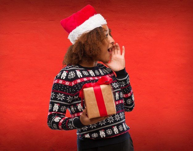 Photo young black woman holding a gift in christmas day whispering gossip undertone