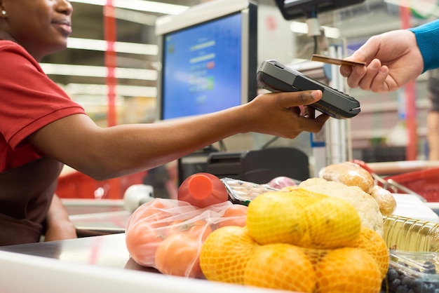 Young black woman holding payment terminal while buyer holding credit card