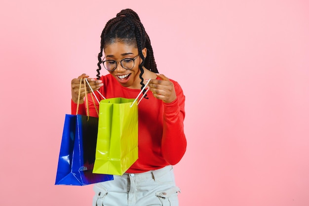 Young black woman holding shopping bags on pink backgrond