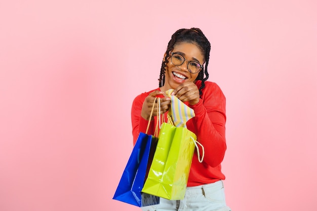 Young black woman holding shopping bags on pink backgrond