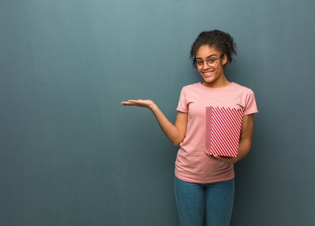 Young black woman holding something with hand. She is holding a popcorns bucket.