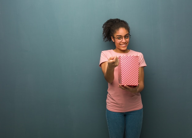 Young black woman inviting to come. She is holding a popcorns bucket.