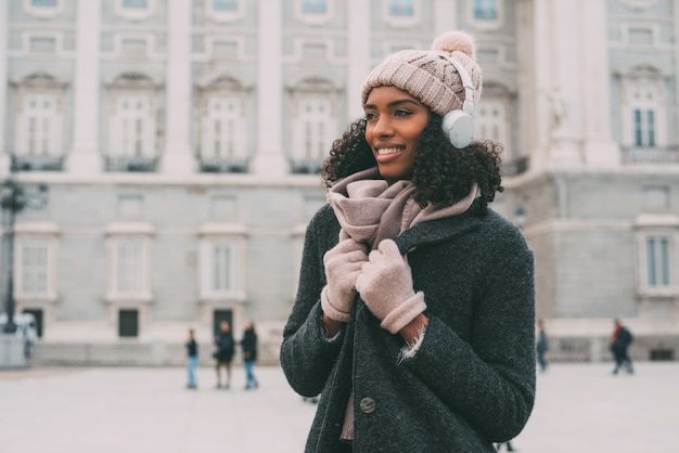 Young black woman listening to music and dancing on the mobile phone near the royal palace in winter