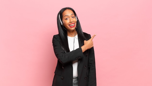 Young black woman looking excited and surprised pointing to the side and upwards to copy space. telemarketing concept