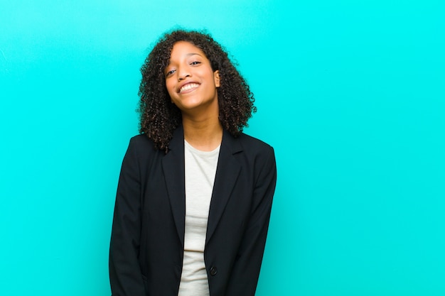 Young black woman looking happy and goofy with a broad, fun, loony smile and eyes wide open against blue wall