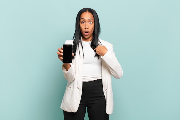 ショックを受けて驚いた若い黒人女性は、口を大きく開いて自分を指しています。スマートフォンのコンセプト