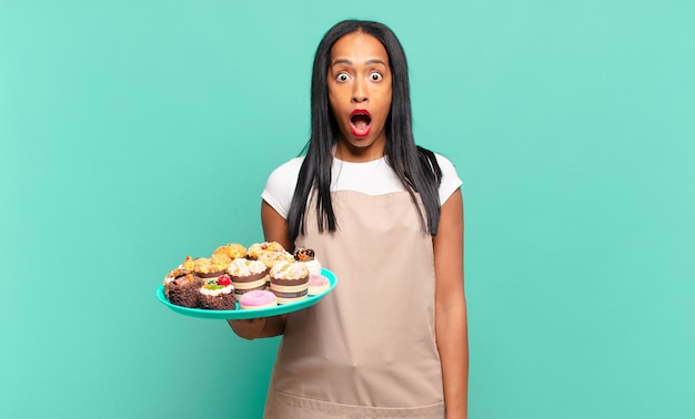 Giovane donna di colore che sembra molto scioccata o sorpresa, fissando con la bocca aperta dicendo wow. concetto di chef di panetteria