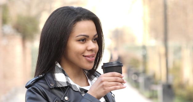 Young black woman outdoors drinking coffee reusalble cup walking city.