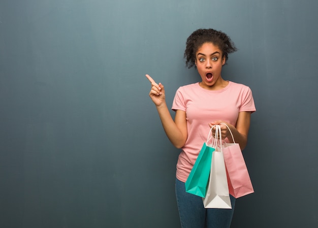 Young black woman pointing to the side. She is holding a shopping bags.
