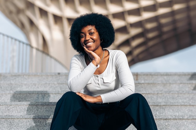 Young black woman posing sitting on a staircase in the street with her head resting on her hand