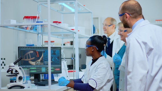 Young black woman scientist doing medical research in modern equipped lab. Multiethnic team examining virus evolution using high tech for scientific analysis of treatment development against covid19.