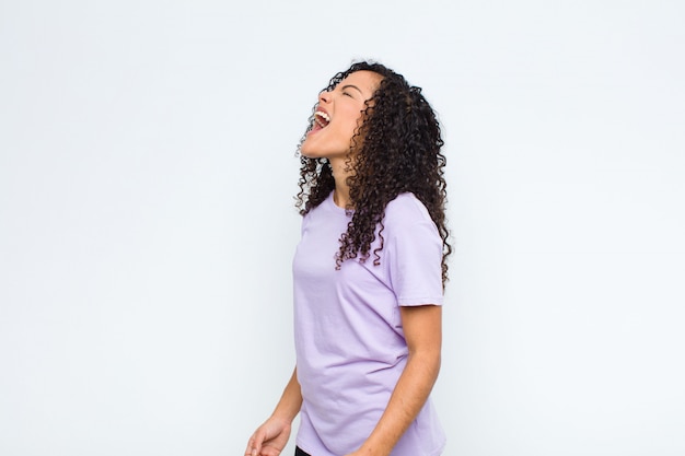 Young black woman screaming furiously, shouting aggressively, looking stressed and angry on white wall