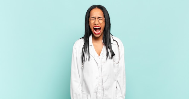 Young black woman shouting aggressively, looking very angry, frustrated, outraged or annoyed, screaming no. physician concept