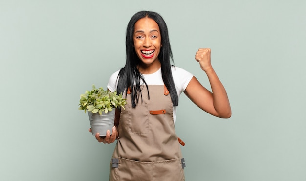 Young black woman shouting aggressively with an angry expression or with fists clenched celebrating success. gardener concept