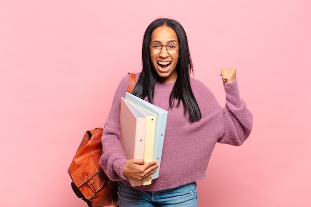 Young black woman shouting aggressively with an angry expression or with fists clenched celebrating success. student concept