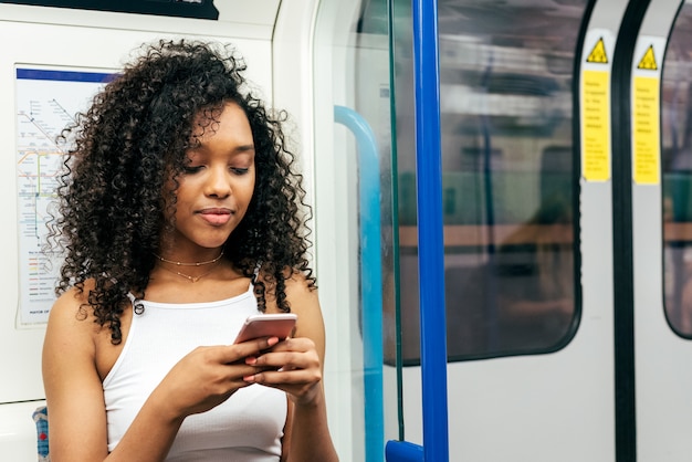 Young black woman sitting inside the underground on the mobile phone
