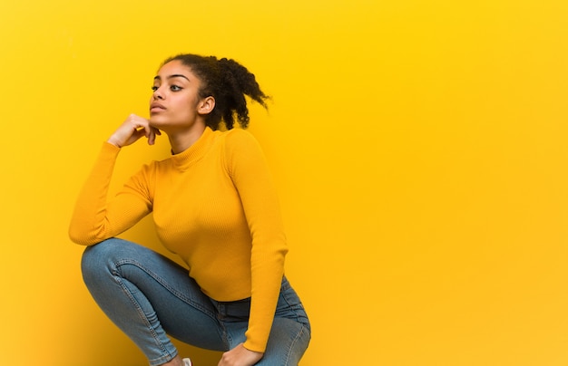 Young black woman sitting over an orange wall