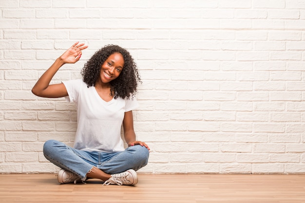 Young black woman sitting on a wooden floor cheerful and confident doing ok gesture