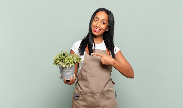 元気に笑って、幸せを感じて、横と上を指して、コピースペースにオブジェクトを表示している若い黒人女性。庭師の概念