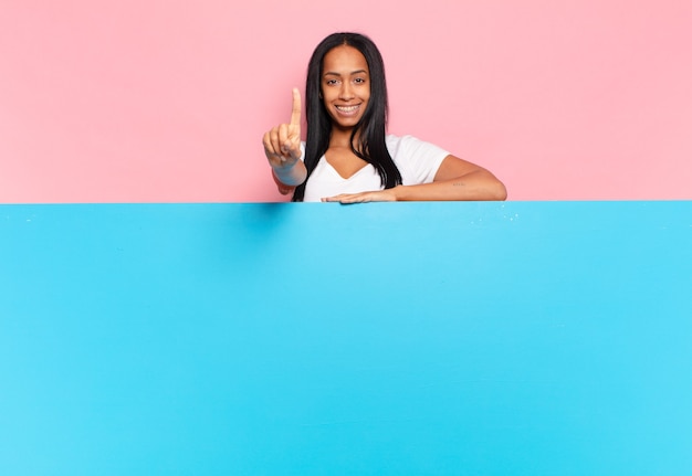 Giovane donna di colore sorridente e dall'aspetto amichevole, mostrando il numero uno o prima con la mano in avanti, conto alla rovescia. copia il concetto di spazio