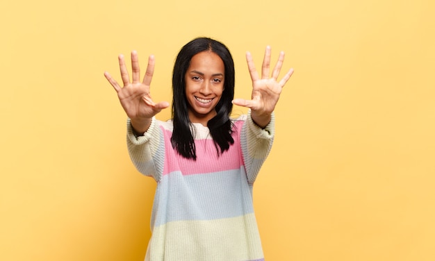 Young black woman smiling and looking friendly, showing number ten or tenth with hand forward, counting down