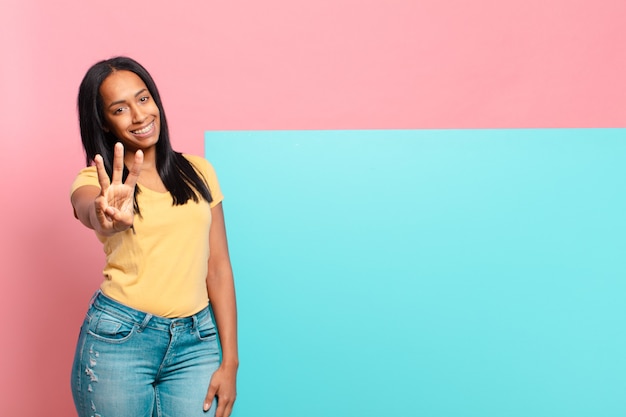 Young black woman smiling and looking friendly, showing number three or third with hand forward, counting down. copy space concept