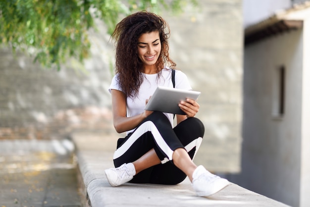 Giovane donna di colore in abiti sportivi facendo uso della compressa digitale all'aperto