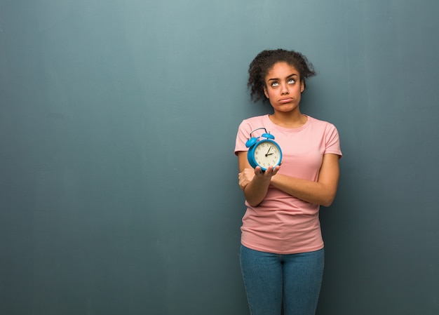 Young black woman tired and bored. She is holding an alarm clock.
