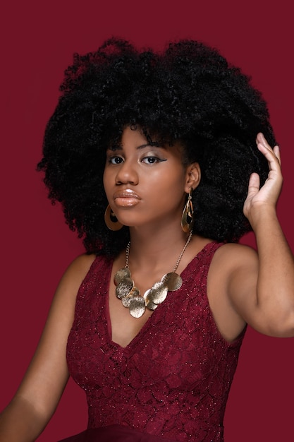 Young black woman touches her hand in afro ben care hair with a red dress isolated on red background