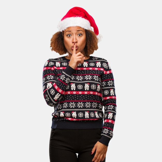 Молодая негритянка в модном рождественском свитере с принтом хранит в секрете или просит молчать