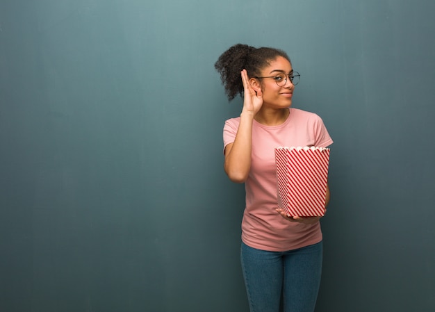 Young black woman try to listening a gossip. She is holding a popcorns bucket.