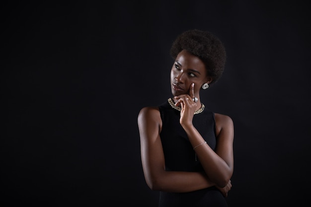 Young black woman trying to find best solution and searching answer african american female having doubtful expression looking side away and holding her chin with hand on black background