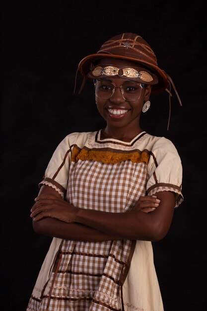 Young black woman wearing glasses and party dress with\
cancageiro hat and studio photo with black background festa\
junina