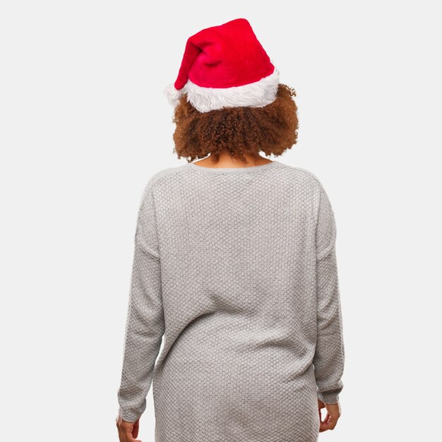 Young black woman wearing a santa hat from behind, looking back